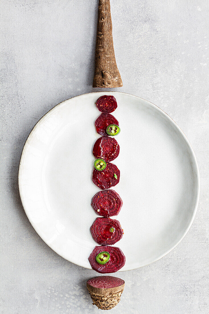 Overhead creative composition of sweet beet slices arranged in line on white plate with vegetable root and tail on sides
