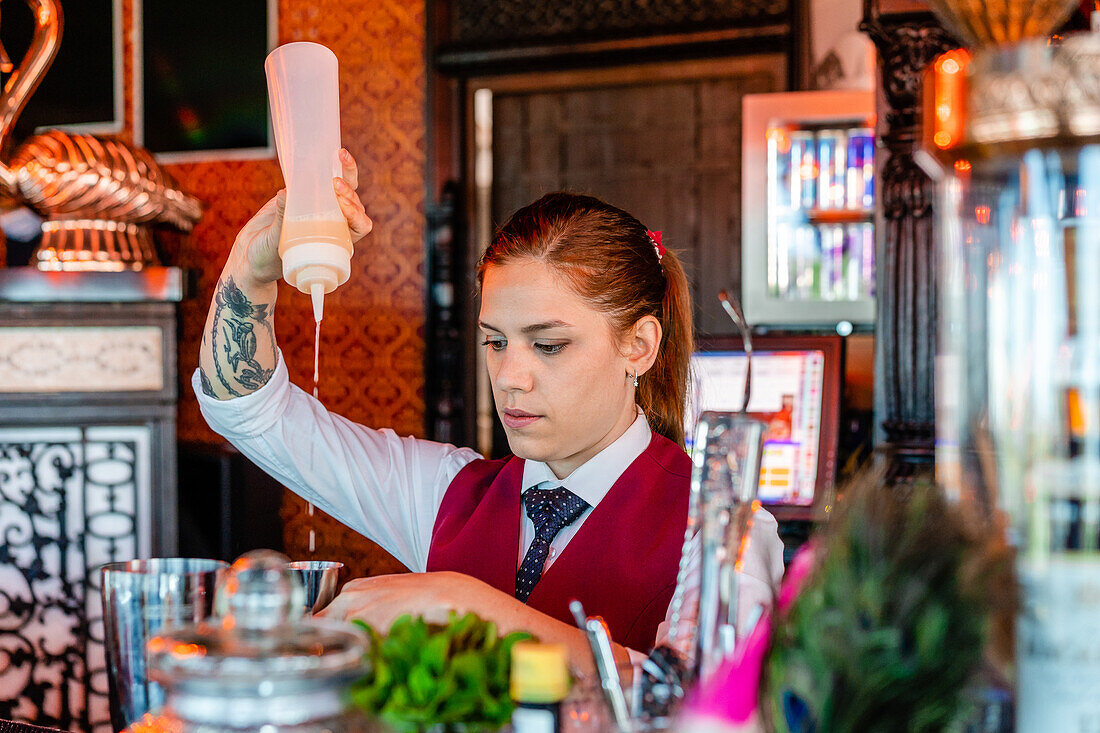Seriöse Barkeeperin in Uniform steht am Tresen einer Bar und gießt Alkohol in einen Shaker, während sie einen Cocktail zubereitet