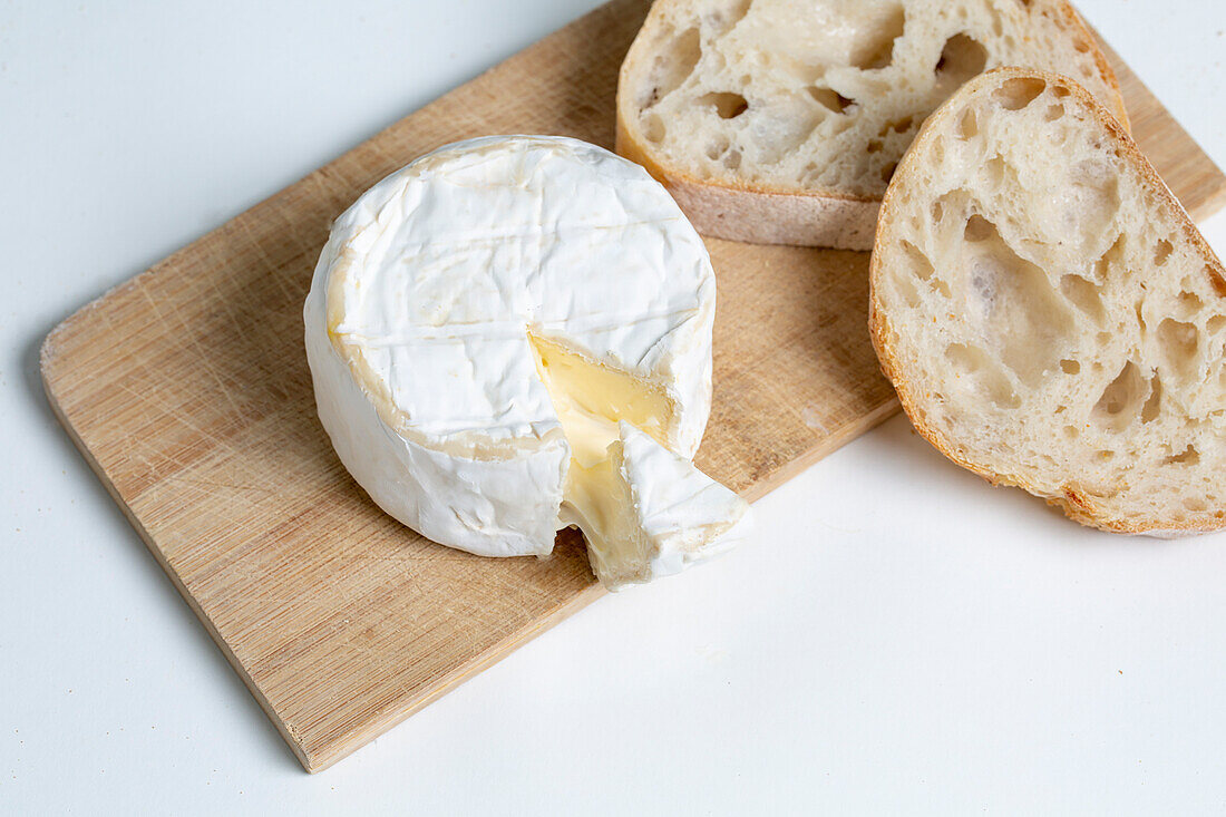 Von oben köstlicher Camembert-Käse auf hölzernem Schneidebrett neben Brotscheiben auf weißem Hintergrund