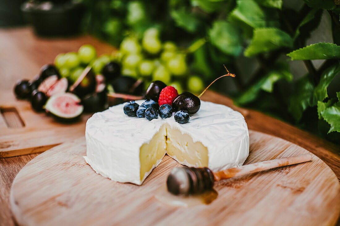 Frischer Camembert-Käse unter reifen Blaubeeren und Kirschen auf Holzbrett mit Honiglöffel