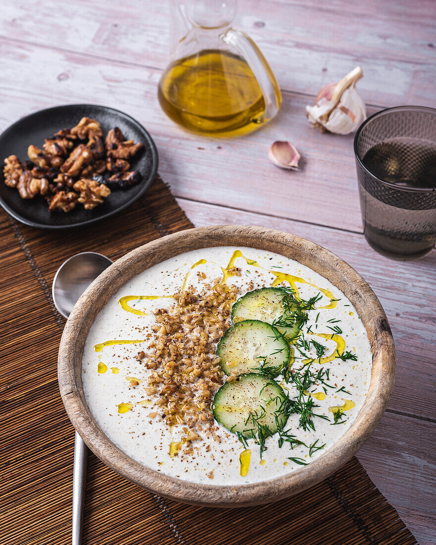 Schüssel mit traditioneller bulgarischer kalter Sommersuppe Tarator mit Joghurt neben einem Glas Wasser und einem Teller mit Nüssen von oben