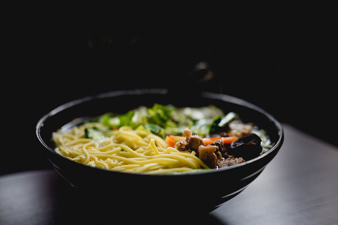 Bowl of savory Asian soup with noodles against dark background in cafe