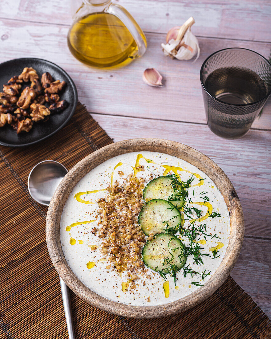 Schüssel mit traditioneller bulgarischer kalter Sommersuppe Tarator mit Joghurt neben einem Glas Wasser und einem Teller mit Nüssen von oben