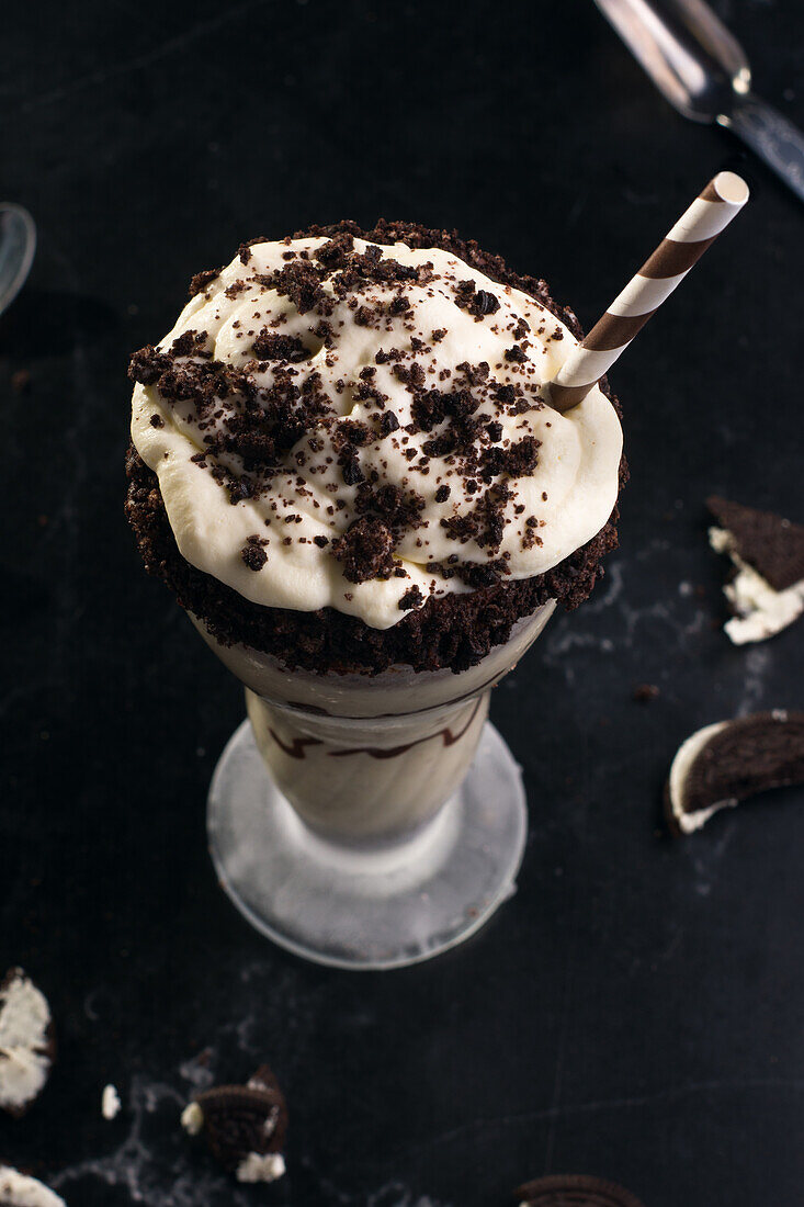 Blick von oben auf leckeren Milchshake mit zerstoßenen Keksen und Strohhalm im Glas mit Schokoladensoße