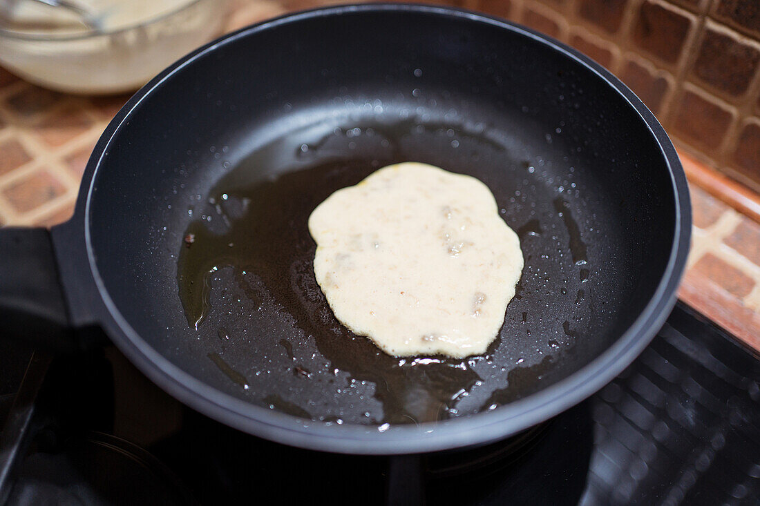 Leckerer hausgemachter Pfannkuchen in einer Pfanne mit Öl auf dem Herd neben einer Glasschale in der Küche