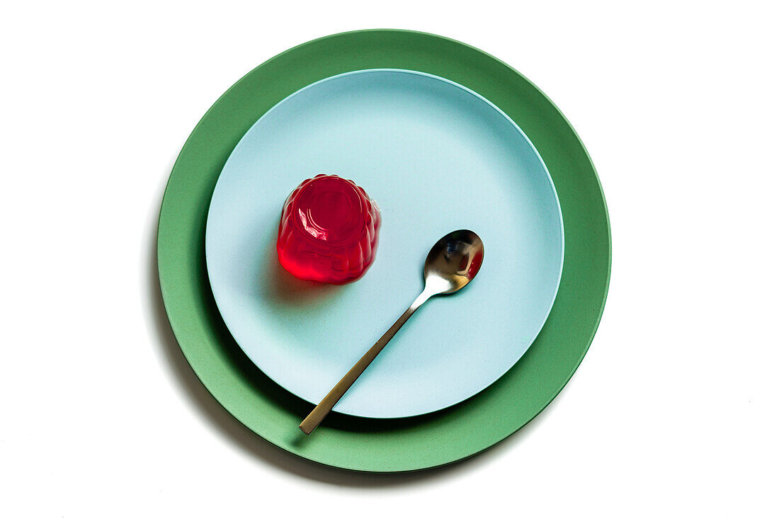 Draufsicht auf appetitliches rotes Beerengelee auf einem hellblauen runden Teller mit Löffel auf weißer Fläche