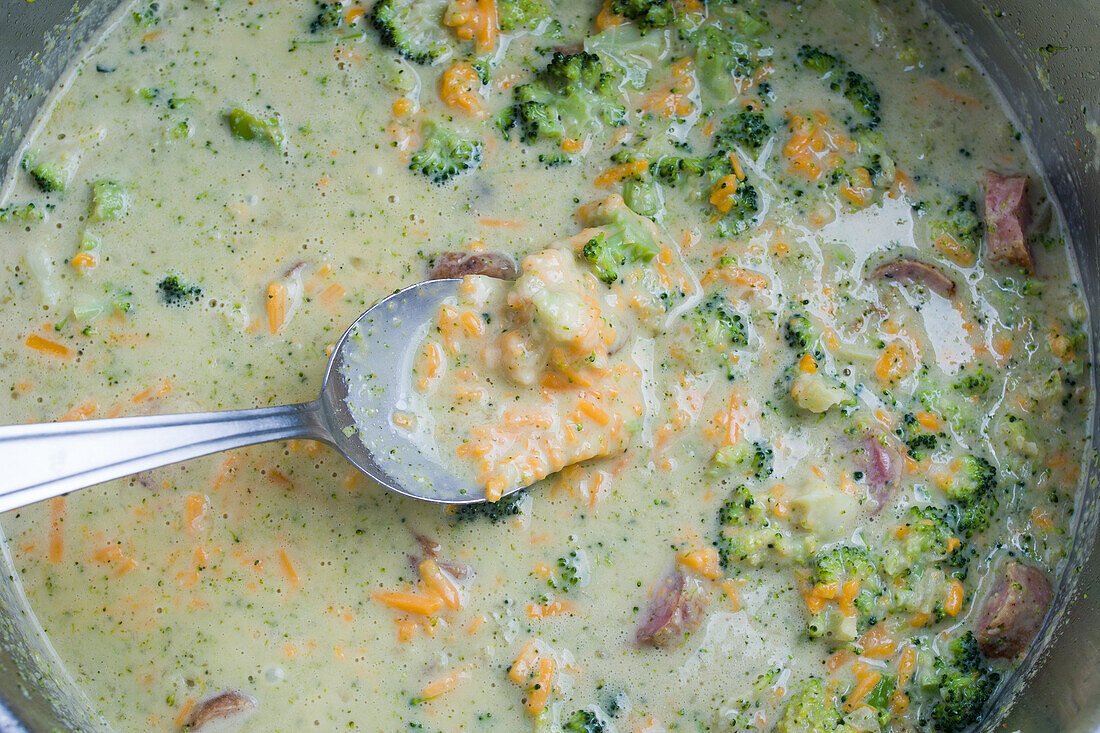 Von oben auf einen Löffel in einer Schüssel mit leckerer Cremesuppe mit Brokkoli und Würstchen