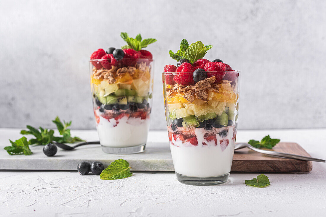 Appetitlicher Joghurt mit Schichten von frischen Früchten, serviert in Gläsern auf einem Tisch mit Minzblättern