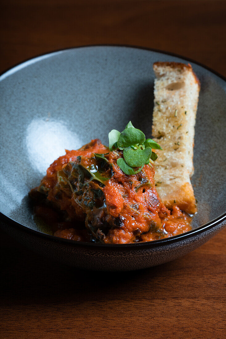 Eine herzhafte Schüssel mit Gemüseeintopf mit Grünkohl, Zwiebeln und Tomaten, serviert mit einer Scheibe getoastetem Sauerteigbrot.