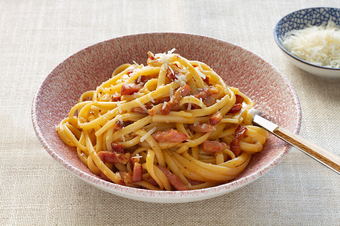 A plate of authentic Italian spaghetti carbonara, garnished with grated cheese and pieces of crispy bacon.