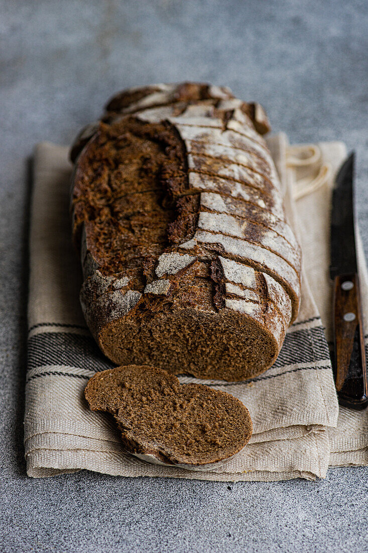 Aufgeschnittenes Roggensauerteigbrot auf einem beigen Tuch mit einem Messer, das die luftige Krume und die knusprige Oberfläche zeigt