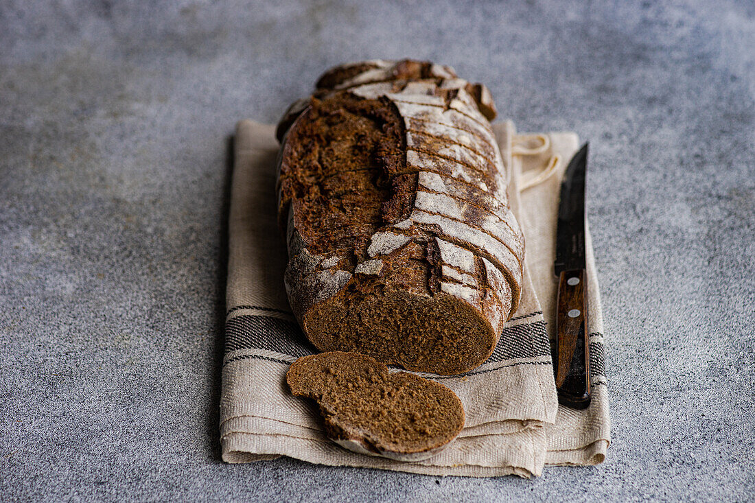 Aufgeschnittenes Roggensauerteigbrot auf einem beigen Tuch mit einem Messer, das die luftige Krume und die knusprige Oberfläche zeigt