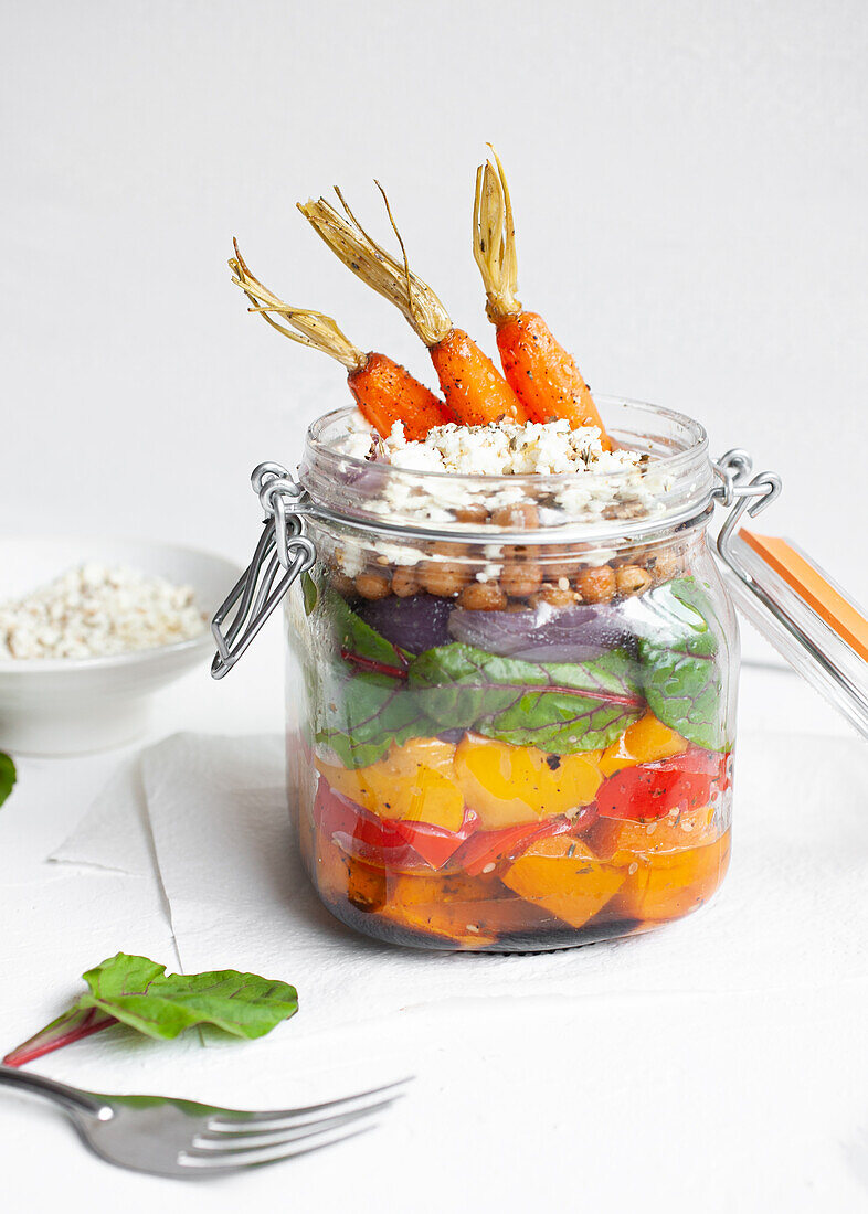 Salat mit bunten, reifen, gehackten Paprikaschoten und Bulgur mit rohen Karotten in einem Glas auf einem Tisch vor weißem Hintergrund