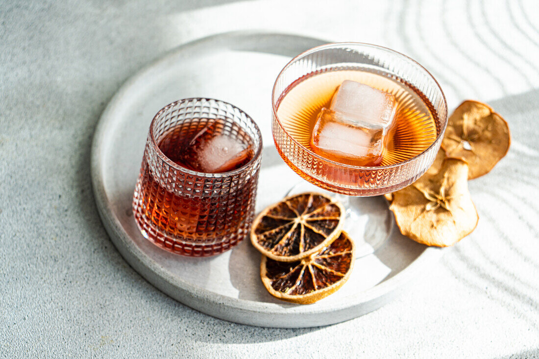 Eine gut beleuchtete, elegante Präsentation verschiedener alkoholischer Getränke in gerippten Gläsern, akzentuiert mit Eiswürfeln und getrockneten Zitrusfrüchten auf einem runden Tablett