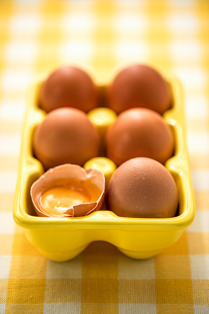 Brown eggs in an egg carton, one egg cracked