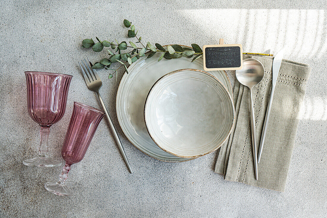 Stylish table setting with vintage-inspired glassware, cutlery, and plates, accented by natural greenery