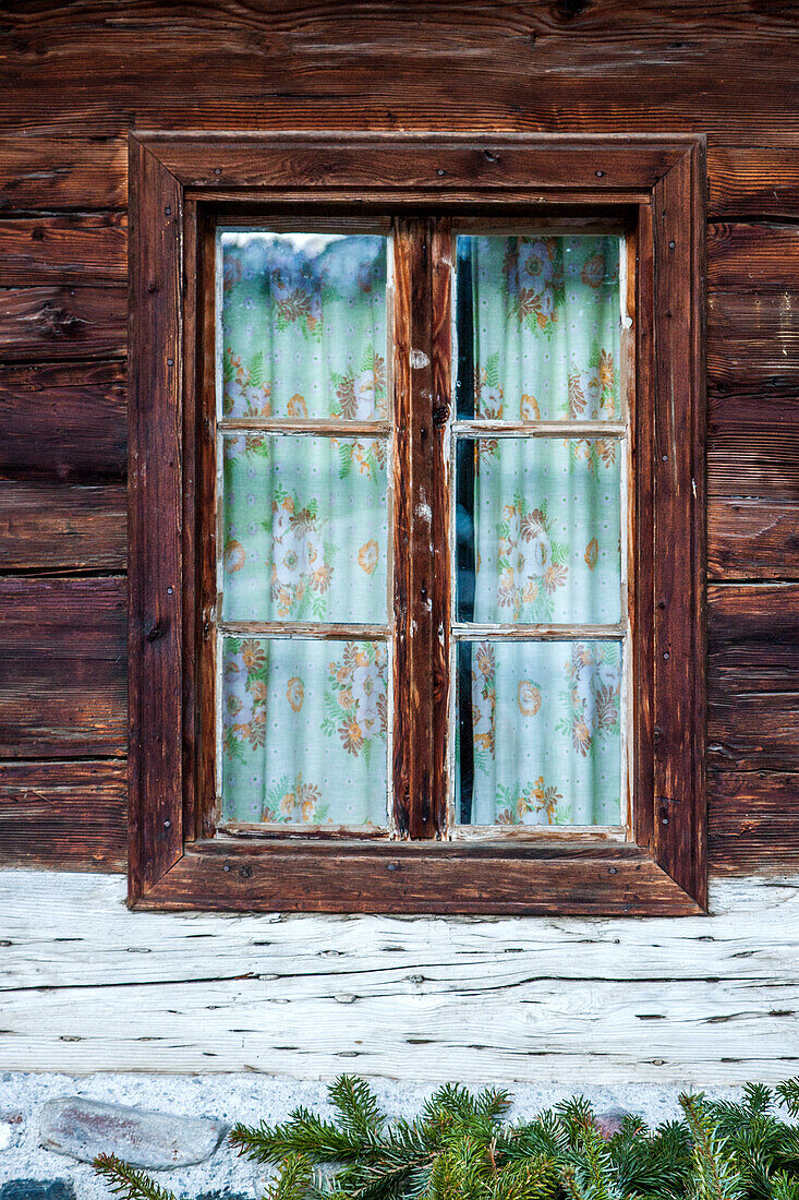 Fenster mit gemusterten Vorhängen im Holzhaus