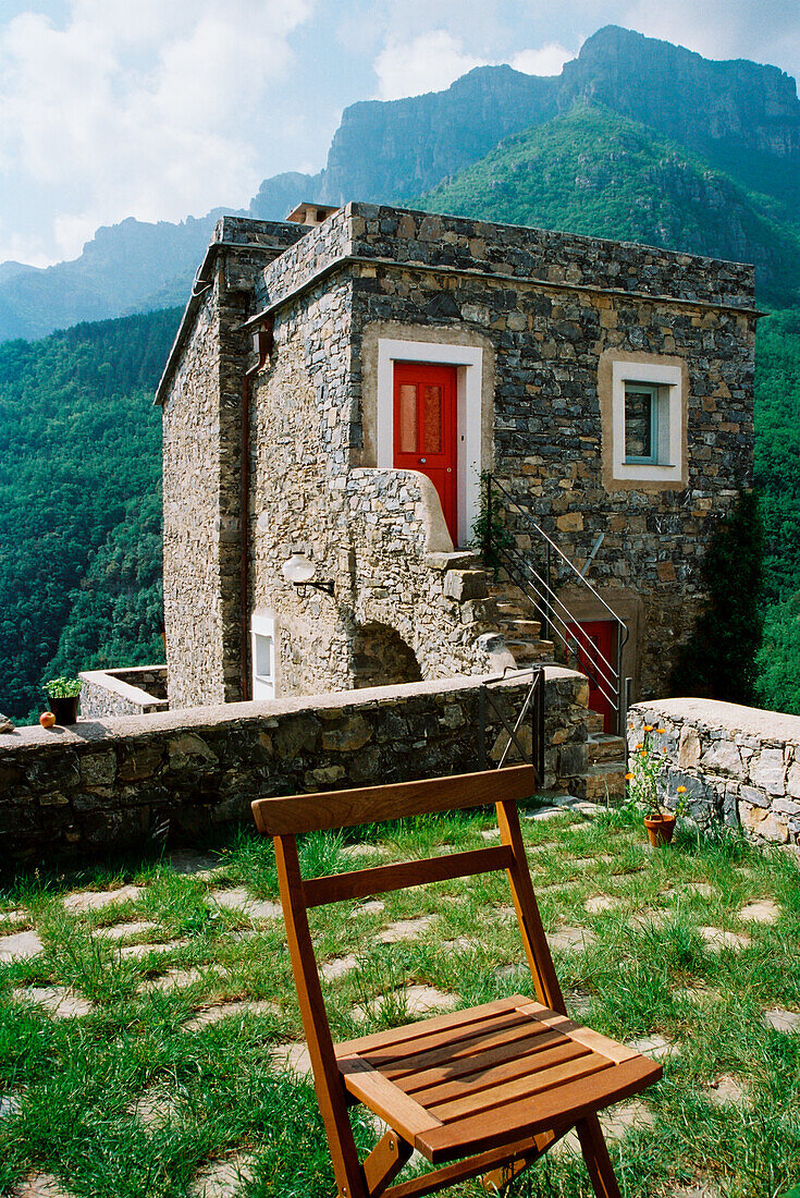 Stone house with red door and garden chair against a mountain backdrop