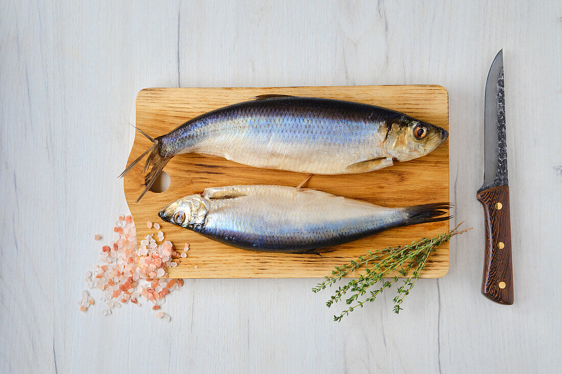 Raw herrings on wooden board with herbs