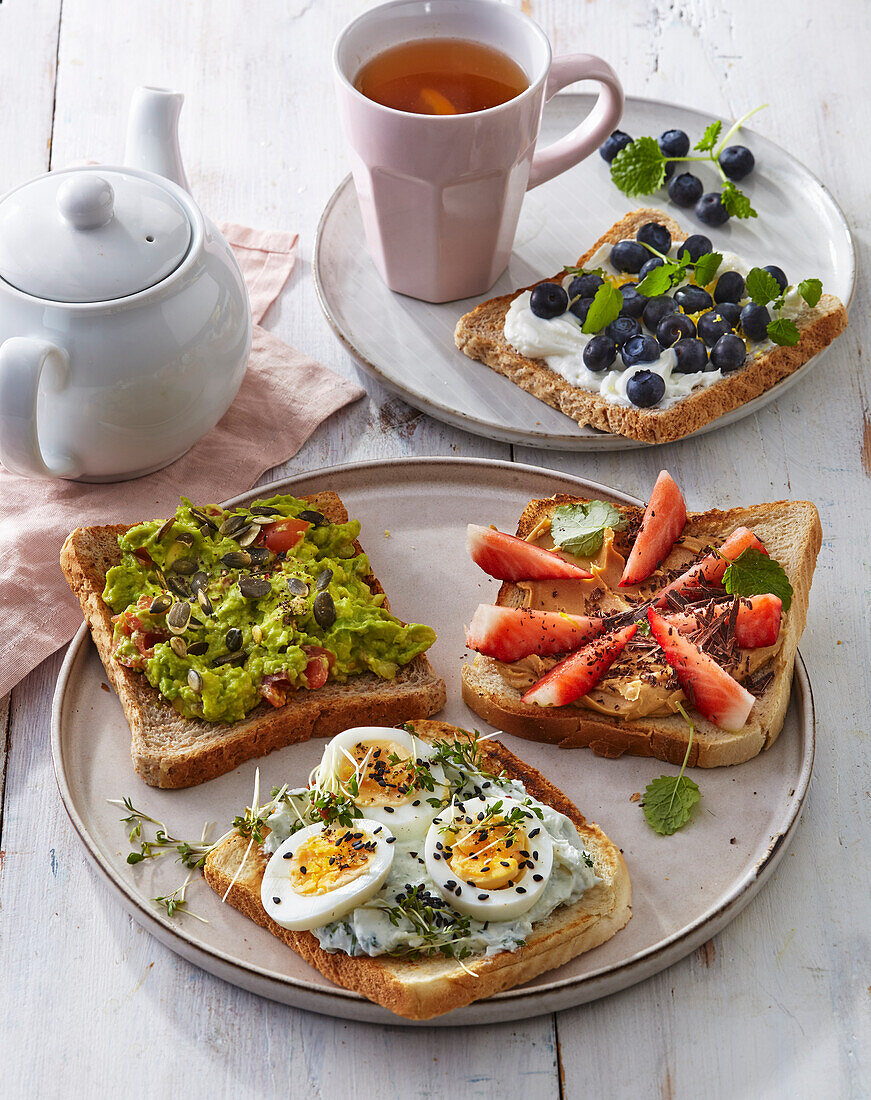 Verschieden belegte Toasts mit Avocado, Ei und Früchten