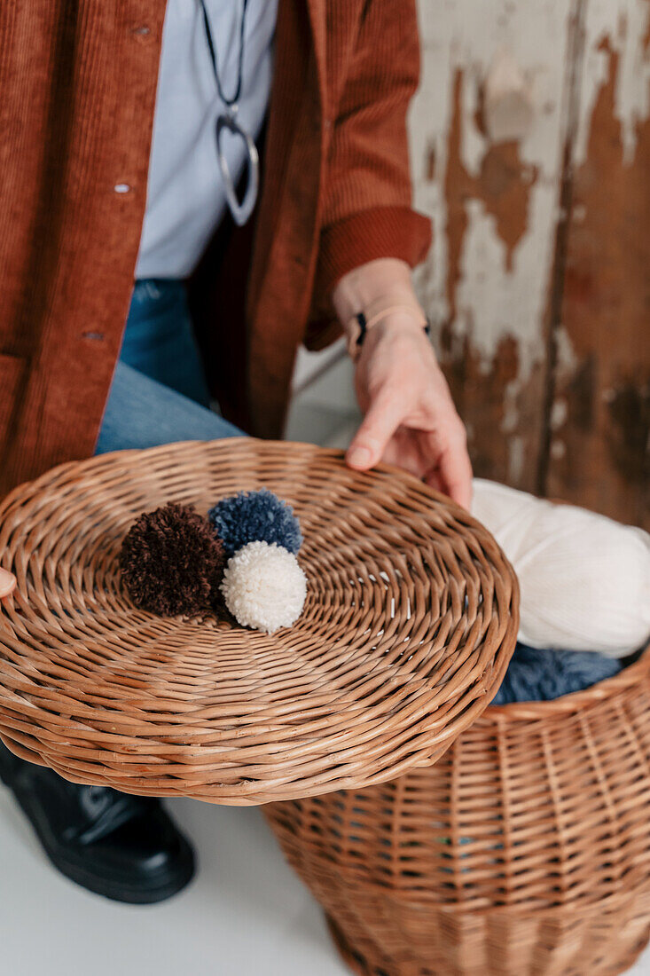 Person hält Korbdeckel mit selbstgemachten Pompons aus Wolle