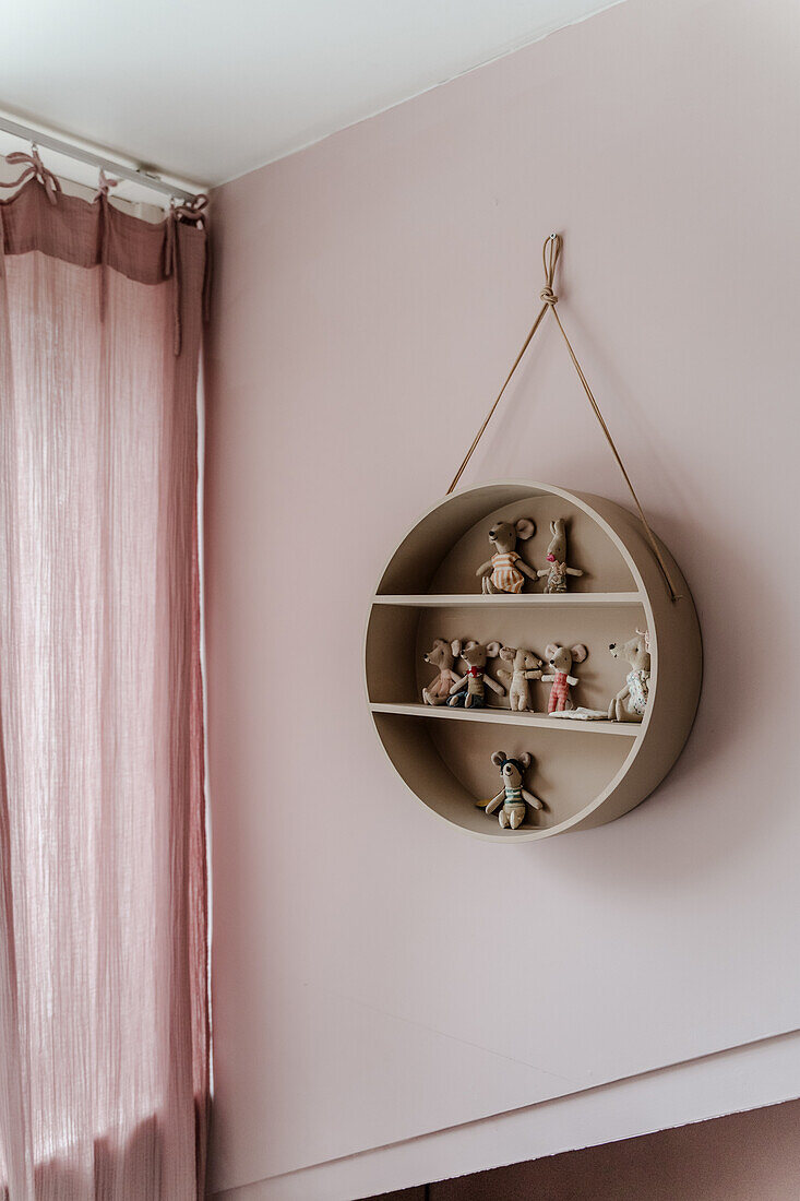 Round wall shelf with doll figures on pink wall in children's room