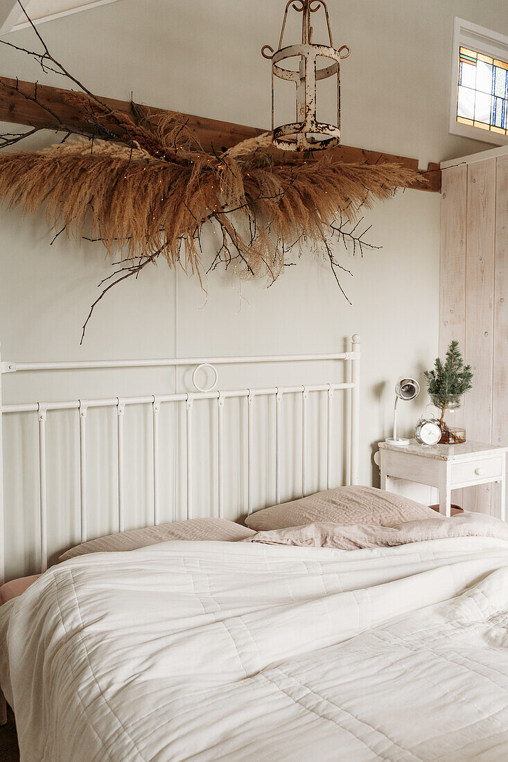 Weißes Metallbett mit Trockenblumen-Dekoration und Nachttisch im Schlafzimmer