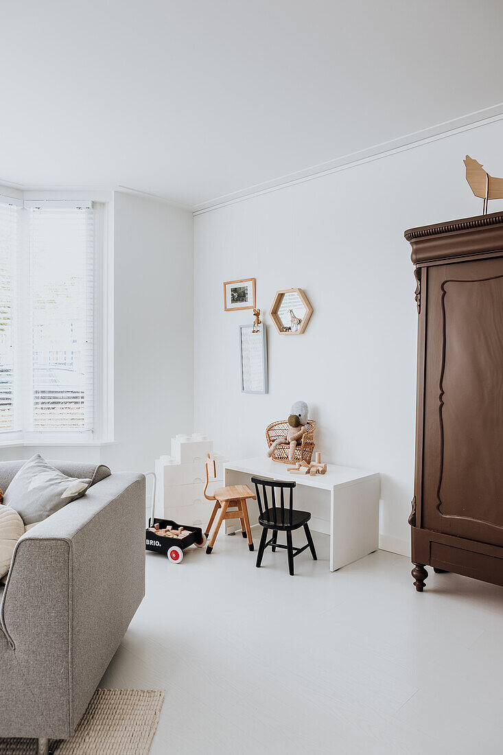 Children's corner with toys, small table and chairs in living room with white wall and wooden cupboard