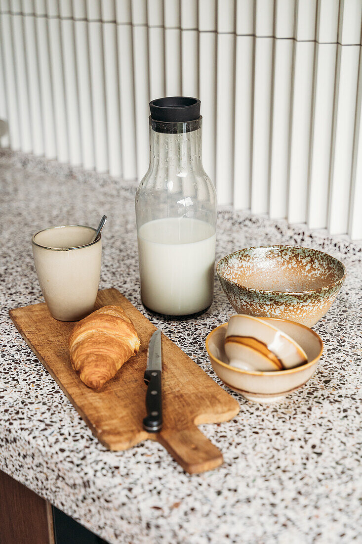 Breakfast arrangement with croissant, milk bottle and ceramic crockery on the kitchen worktop