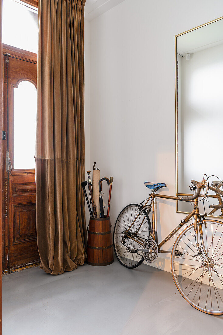 Hallway with wooden umbrella stand and bicycle in front of large mirror