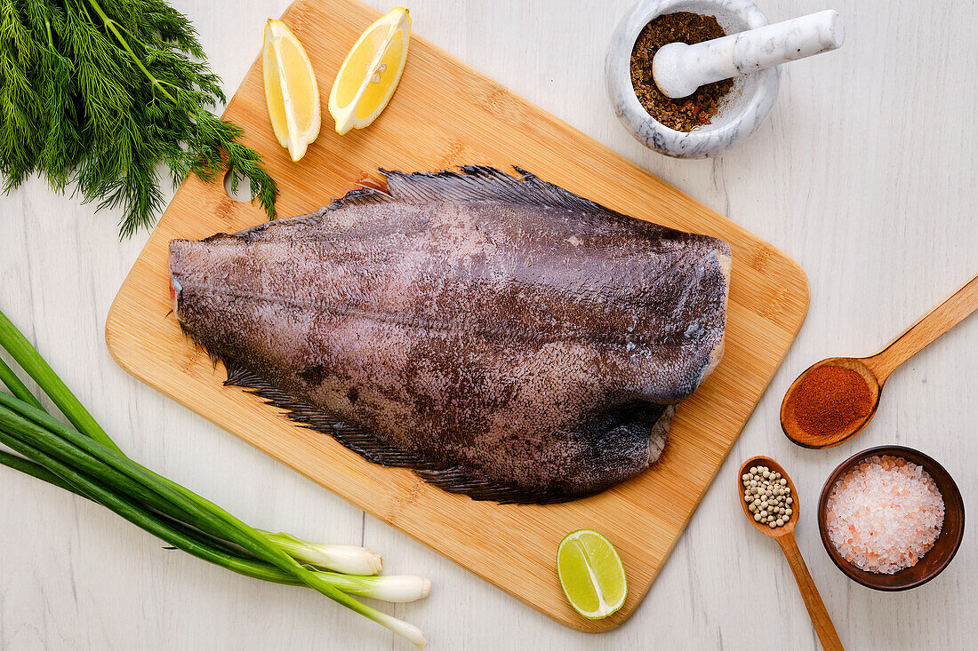 Raw halibut on a wooden board with spices and lemon