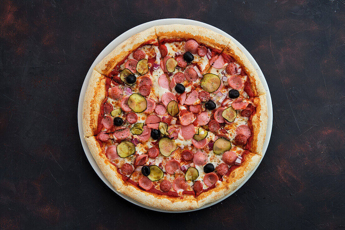 Pizza with various types of sausage, gherkins, olives and onions