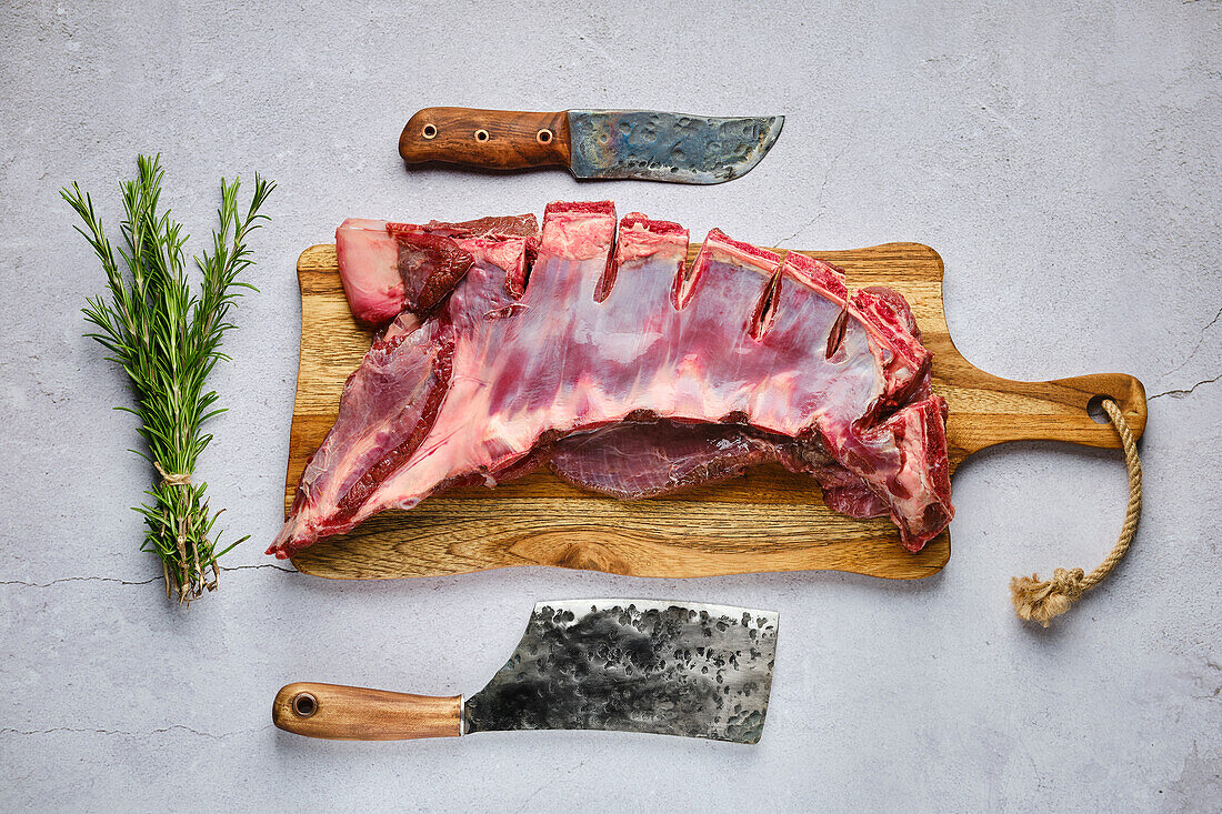 Raw venison ribs on cutting board with rosemary and knives