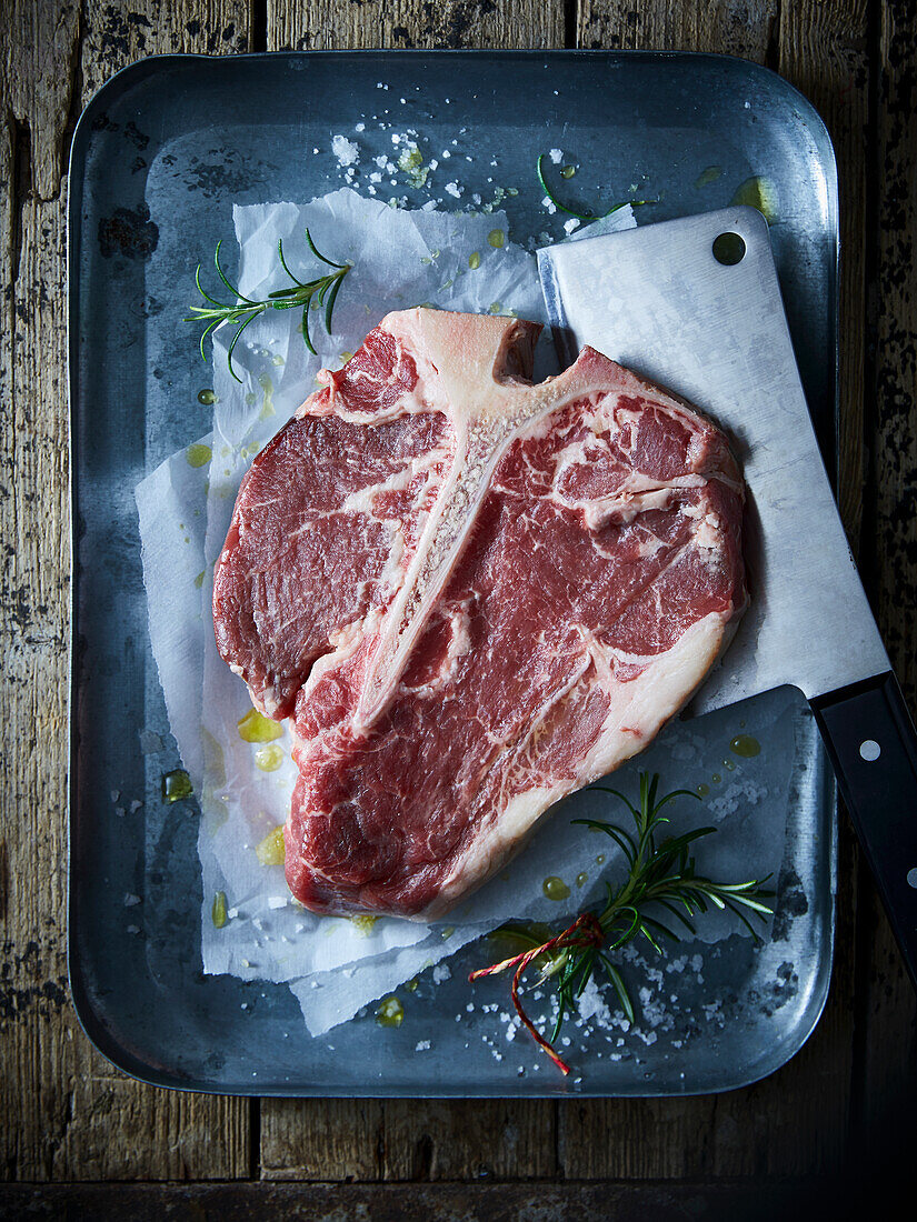 T-bone steak with rosemary and sea salt on a baking tray