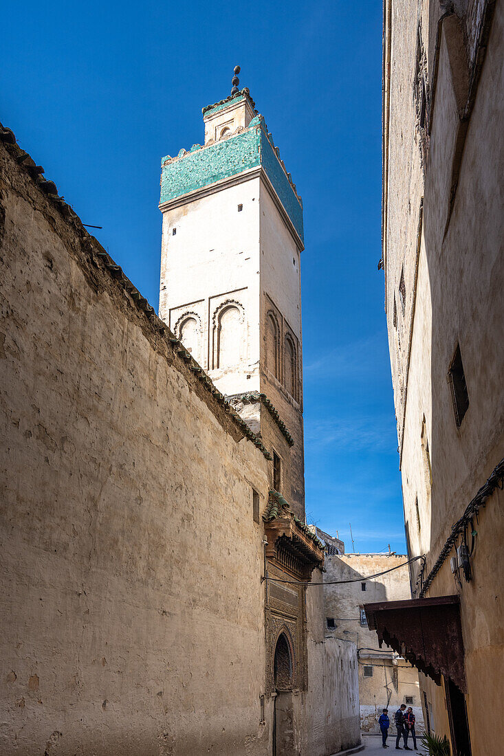 The towering minaret of Bensouda Mosque rises above Fezs ancient medina under a clear sky. Fez, Morocco.