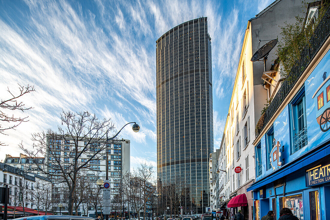 The towering Montparnasse skyscraper stands against a dusk sky in bustling Paris.