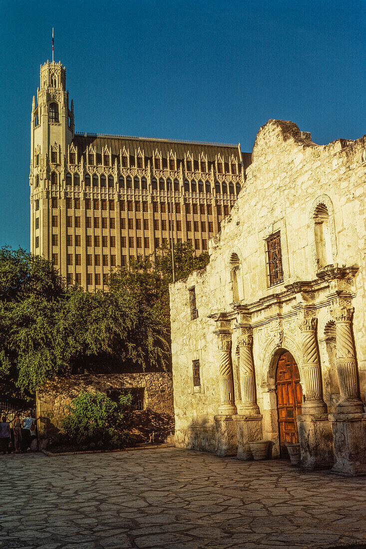 Der historische Alamo auf der Alamo Plaza mit dem dahinter liegenden Emily Morgan Hotel in San Antonio, Texas. Das Emily Morgan Hotel wurde 1924 als Medical Arts Building erbaut.