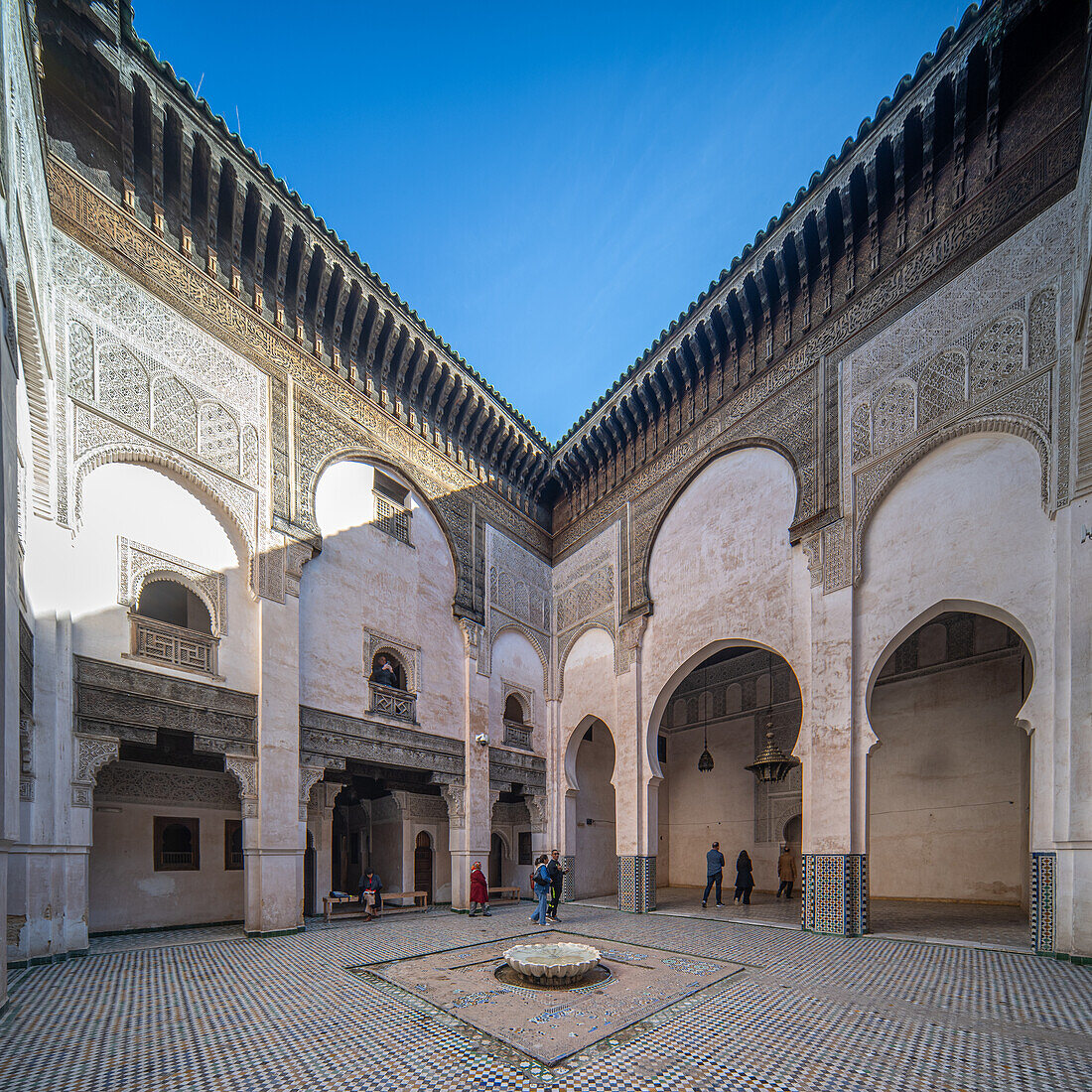 visitors in the ornate courtyard of Madrasa Cherratine under a clear blue sky.