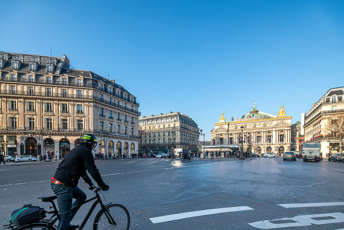 Ein Radfahrer überquert bei strahlend blauem Himmel eine Kreuzung am Pariss Opera Square.