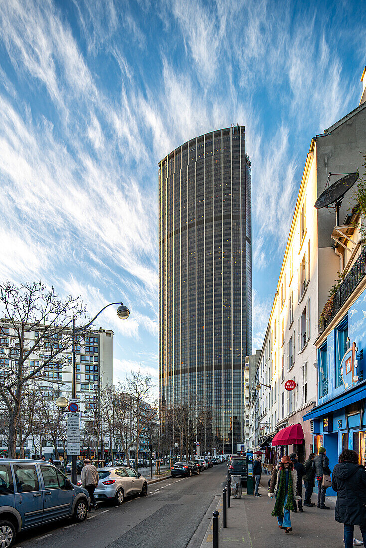 The towering Montparnasse skyscraper stands against a dusk sky in bustling Paris.