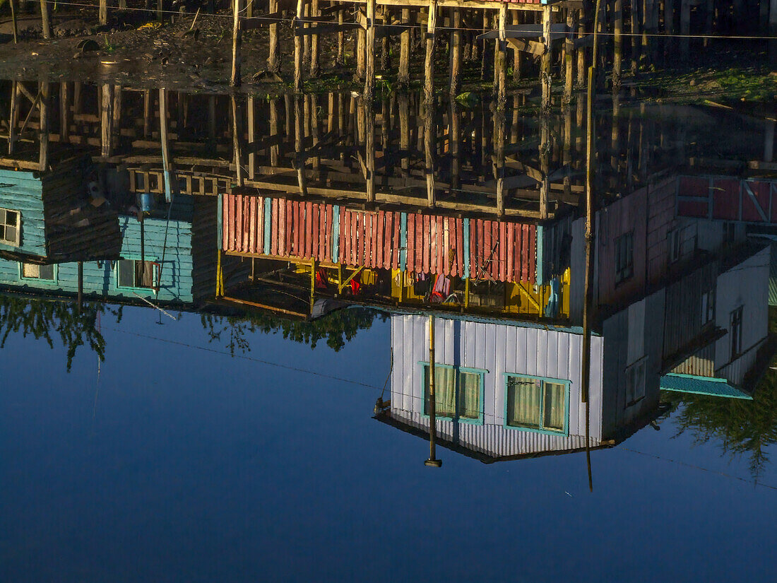 Bunte Palafitos oder Stelzenhäuser der Fischer spiegeln sich bei Sonnenaufgang in einer Bucht in Castro auf der Insel Chiloe, Chile.