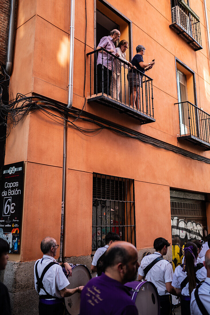 Menschen auf einem Balkon, die den zehnten Aufbruch des Cruz de Mayo, der Maikreuzprozession, der Bruderschaft Jesus el Pobre, Madrid, Spanien, beobachten.