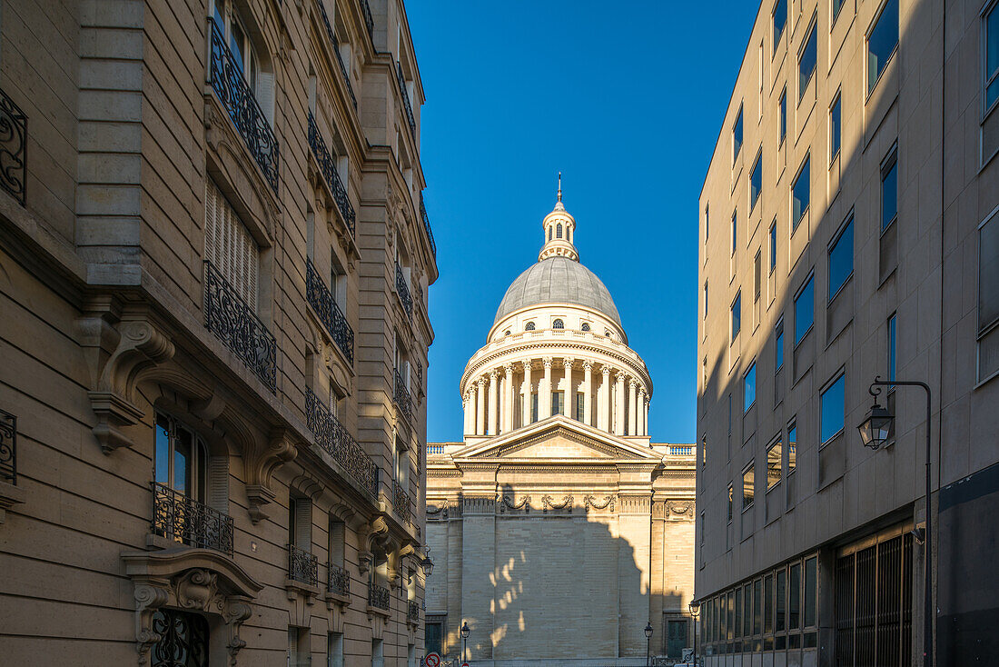 Die große Kuppel des Panthéon hebt sich von einer Pariser Straße aus gesehen gegen einen klaren Himmel ab.