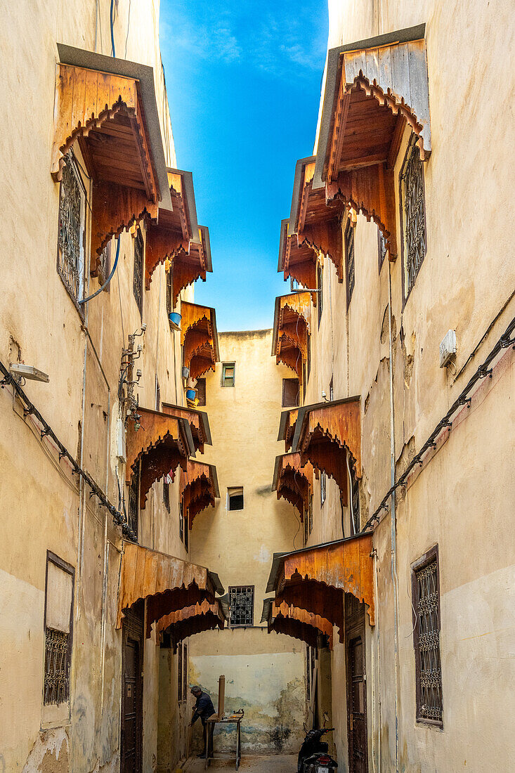 Narrow alley with ornate wooden awnings in Fez medina.