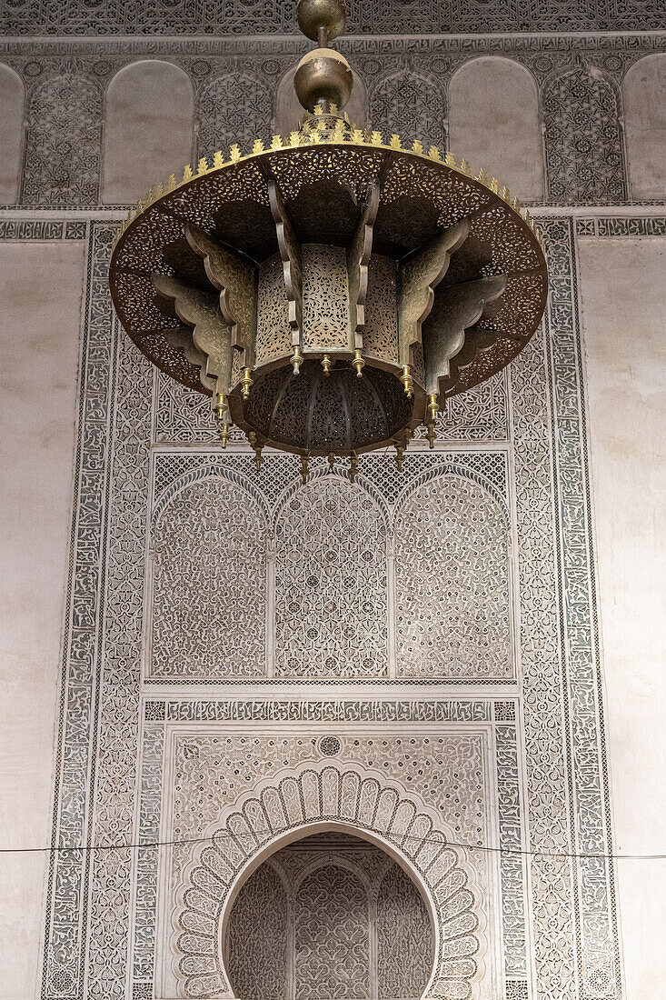 Eine Bronzelampe hängt vor der kunstvoll gefliesten Kulisse der Cherratine Madrasa in Fes, Marokko.