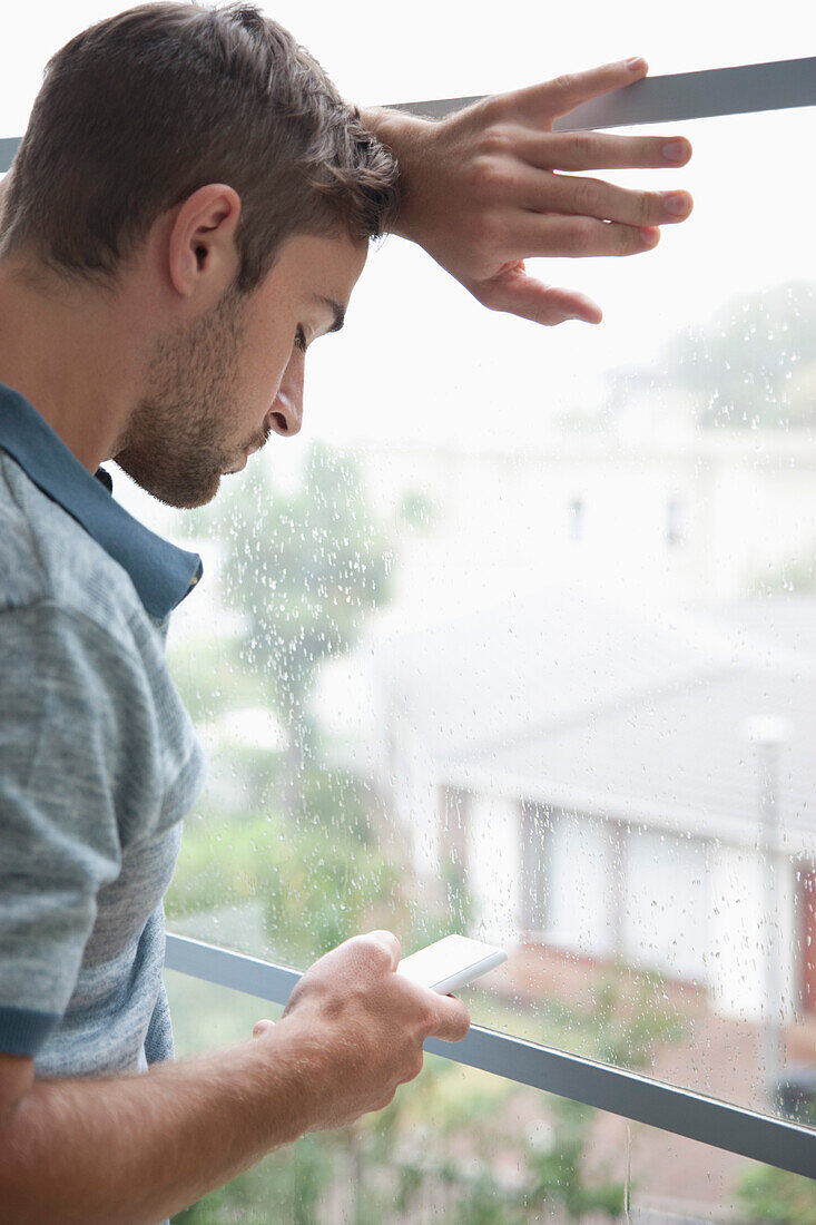 Mann lehnt am Fenster und benutzt Smartphone