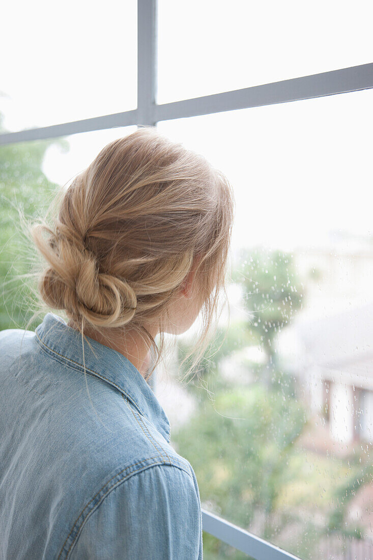 Rückansicht einer Frau, die aus dem Fenster schaut