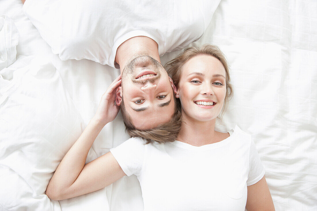 Smiling Couple Lying on Bed Facing Opposite Directions