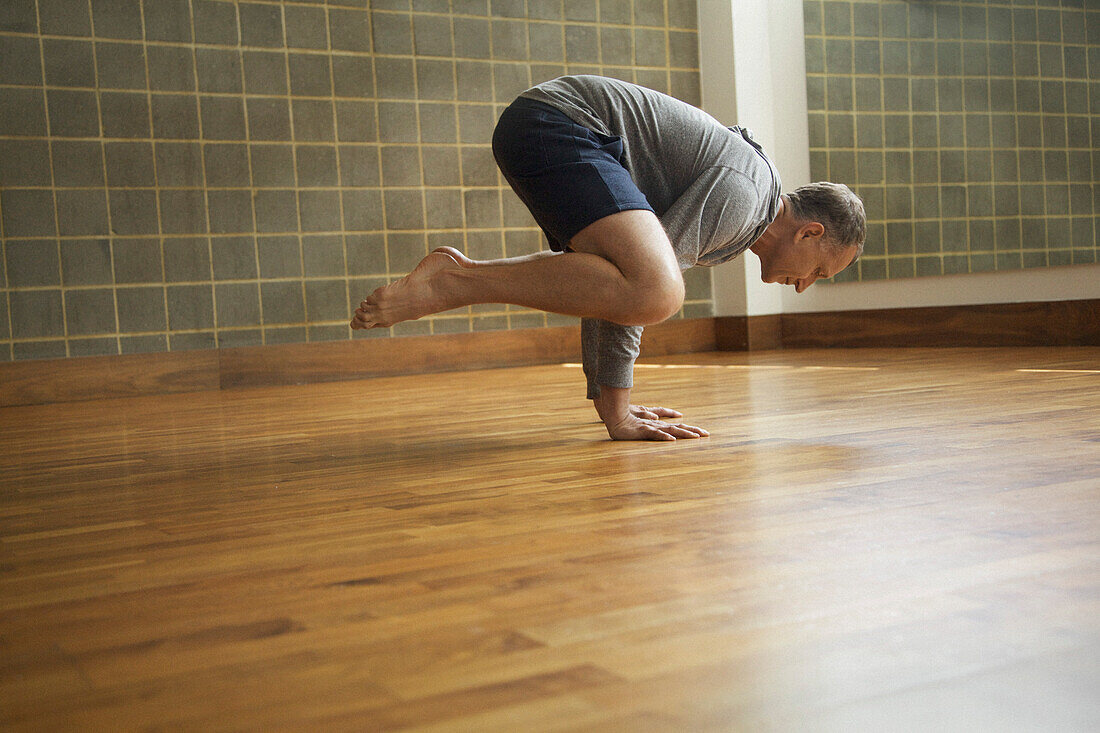 Älterer Mann übt Yoga, Krähenstellung