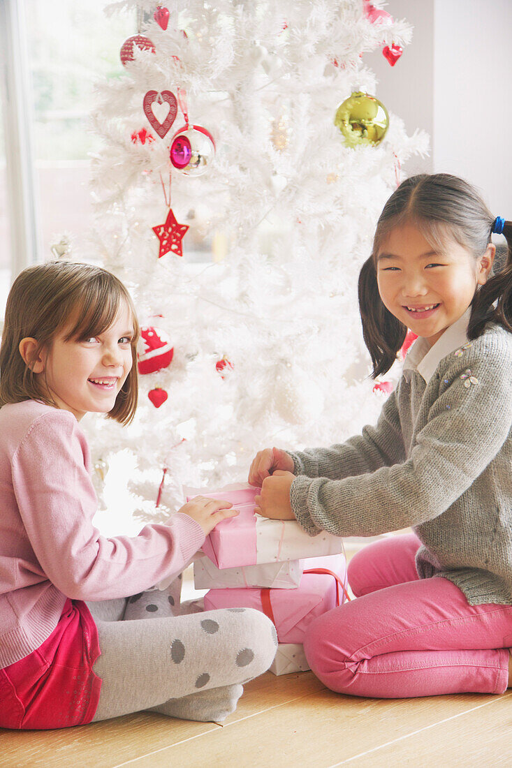 Zwei junge Mädchen öffnen Geschenke unter dem Weihnachtsbaum, lächelnd